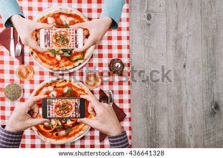 Two people eating a vegetable pizza at the restaurant, they are taking pictures of food with their smartphones