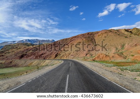 Scenic summer view with the bend of the asphalt road in the mountains of red stone on a background of blue sky and clouds on a sunny day