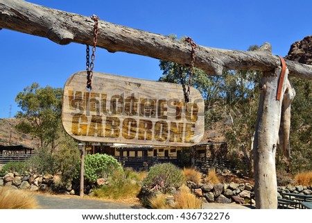old vintage wood signboard with text " welcome to Gaborone" hanging on a branch