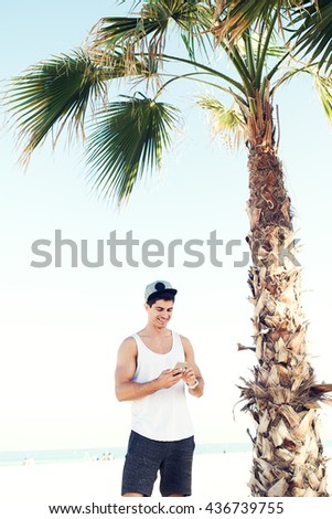 Handsome fashion model looking at smart phone at beach.