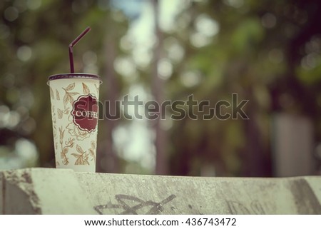 Soft focus on a cup of cool coffee in the park with background is blur of light streaming through leaves at summer time. low depth of field. selective focus. vintage or retro style.