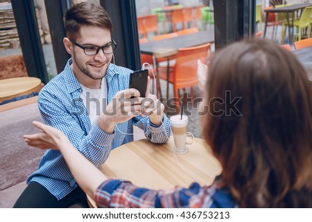 The boy and girl resting in cafe, photographed on the phone and listening to music on headphones