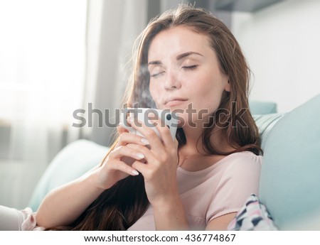 Young woman sitting on couch at home and drinking coffee, casual style indoor shoot Royalty-Free Stock Photo #436774867