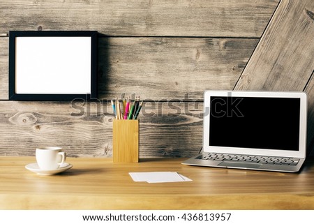 Closeup of creative wooden designer desk with blank laptop screen, picture frame, coffee cup and stationery items. Mock up