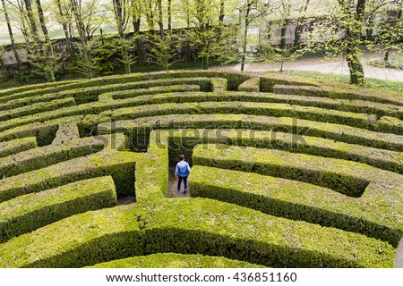 Green bushes labyrinth, hedge maze. A young boy with blue jacket searches the exit. Royalty-Free Stock Photo #436851160