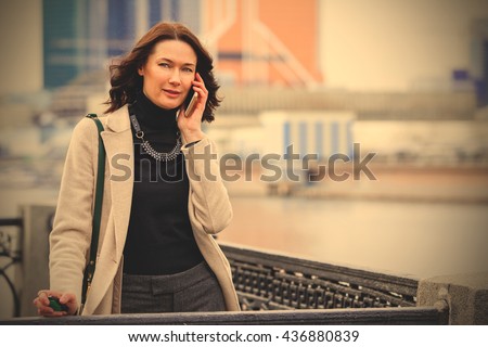 european beautiful middle-aged woman talking on the phone and smiling outdoors. business. fashion. instagram image filter retro style