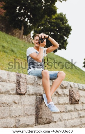 lifestyle happy young guy in sunglasses and a fashionable hairstyle make professional pictures,bearded man,hiker man,holding big camera,man with perfect white teeth,cute smile,shows peace sign,cool