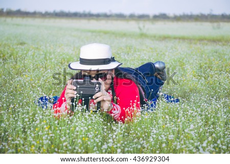 Woman in red shirt and hat lay down on grass meadow take a photo by smartphone