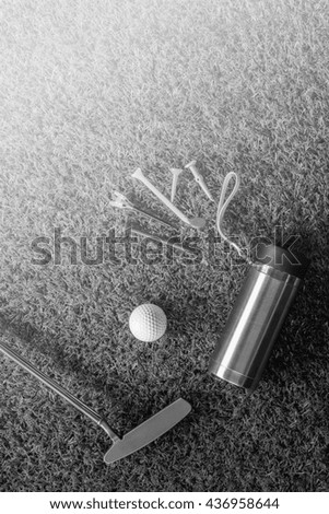 golf accessories ,tees, putter,golf ball and water bottle on green grass..black and white.