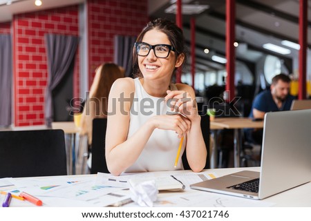 Portrait of smiling pretty young business woman in glasses sitting on workplace Royalty-Free Stock Photo #437021746