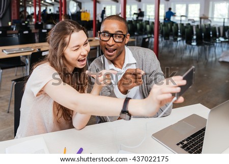Cheerful funny young business people working and taking selfie in office