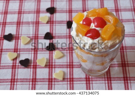 Glass of  dessert vanilla mousses with fruit on top and with white and dark chocolate heart on background.