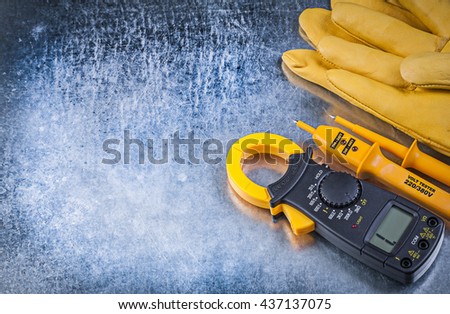 Digital clamp meter electrical tester protective gloves on metallic background electricity concept.