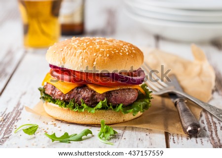 Closeup of a fresh homemade better burger on an old white wooden board with tomato, cheese and red onion.