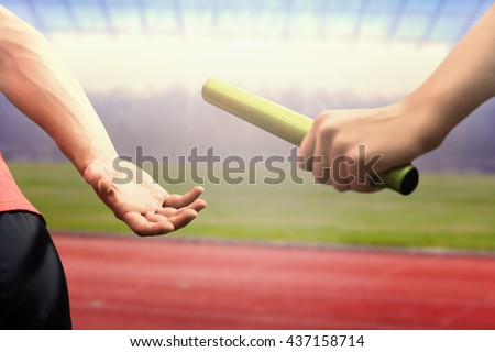Athlete passing a baton to the partner against race track Royalty-Free Stock Photo #437158714
