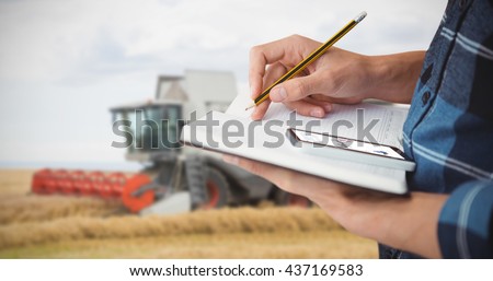 Farmer with pencil on book against view of a harvester