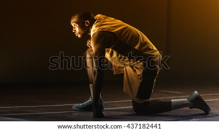 Basketball player preparing to play with knee on the floor and looking up on a gym