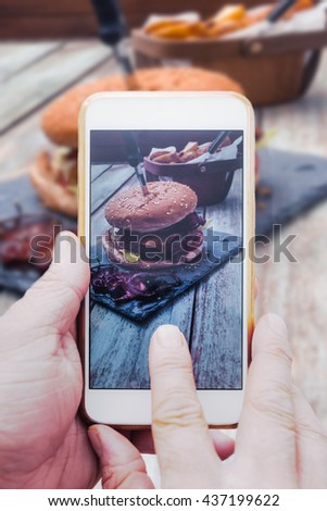 Hand with smart phone, taking picture of  food, bacon cheeseburger with potato cuts on vintage wood  table for sharing online
