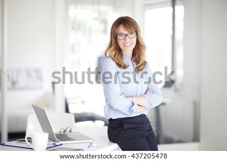 Portrait of successful middle aged businesswoman standing at her office. Royalty-Free Stock Photo #437205478
