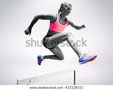 Sporty woman jumping a hurdle against grey background