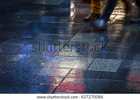 Two people walking in the reflection of neon lights on the wet sidewalk.