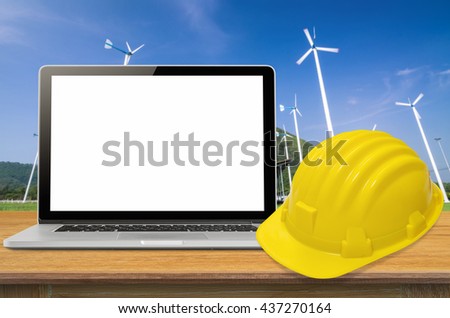 Yellow safety helmet and laptop on desk with industry background, blank on screen.