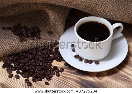 Coffee beans and coffee in white cup on wooden table with burlap. Selective focus.