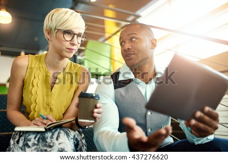 Two creative millenial small business owners working on social media strategy using a digital tablet while sitting in staircase Royalty-Free Stock Photo #437276620