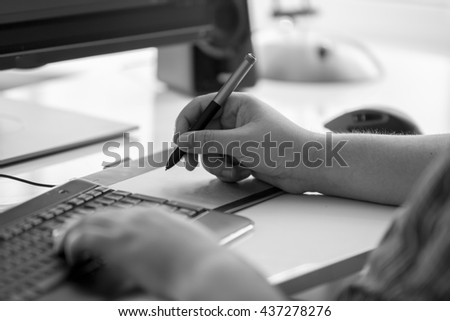 Black and white photo of graphic designer using digital tablet at office