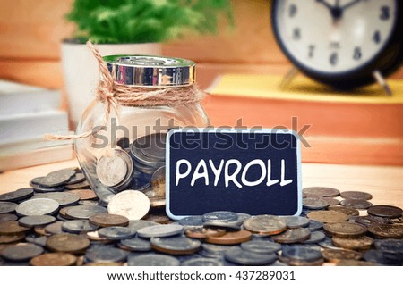 Word Payroll on mini chalkboard and coin in the jar with blurred background of books, green plant and clock. Financial Concept.