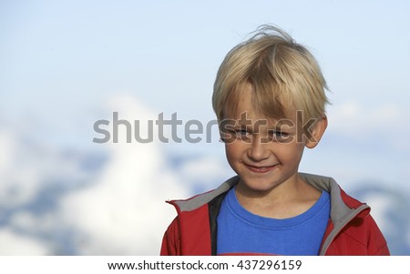 Little blond smiling boy - traveller in Alps (Dolomites) mountains with clouds background