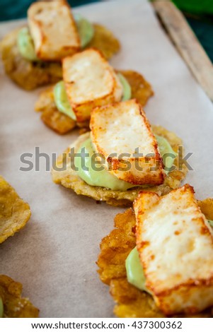 Fried plantain toston (patacon) with fried cheese on greet wood table