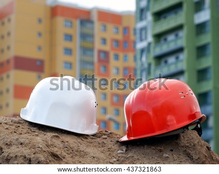 Orange helmet builder and a white helmet engineer on the background buildings. Helmets are a mountain of sand