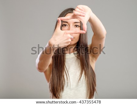 Picture of lovely woman creating a frame with fingers isolated on gray background