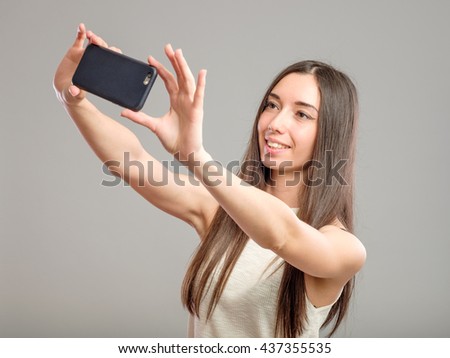 Beautiful woman taking self picture with smartphone camera isolated on gray
