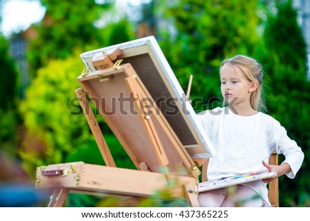 Adorable little girl painting a picture on easel outdoors