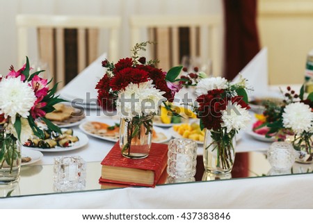 Red and white chrisantames stand in glass vases on books
