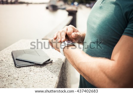 Close-up of a man 's hand with smart watch, uses a smart watch , white strap. on open air. It lies next to a digital tablet and smartphone Royalty-Free Stock Photo #437402683