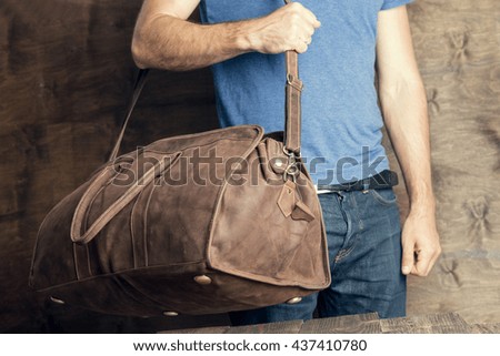Young man with a brown vintage travel bag on his shoulder standing on a dark wooden background