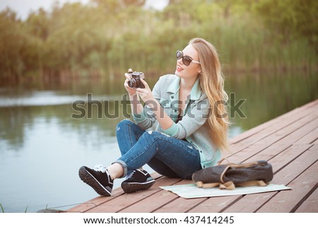 Outdoor summer smiling lifestyle portrait of pretty young woman traveling with camera and making pictures. Young girl tourist in sun glasses making photo