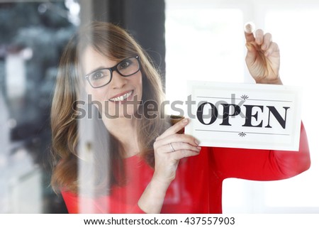Portrait of a smiling middle aged shop assistant holding up a sign on opening day of her small business.
