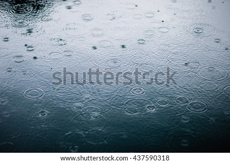 rain drops on the surface of water in a puddle with graduated shade of black shadow and reflection of blue sky  Royalty-Free Stock Photo #437590318