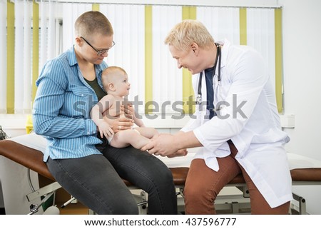 Mother Looking At Happy Mature Doctor Holding Baby's Legs
