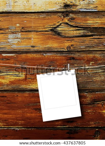 Close-up of one blank instant square photo frame hanged by peg against brown weathered wooden boards background