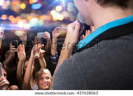 holidays, music, nightlife and people concept - close up of singer singing on stage over happy people crowd taking picture by smartphones and waving hands at concert in night club
