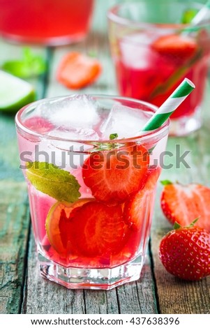 Strawberry lemonade with lime and ice in a glass on a wooden table