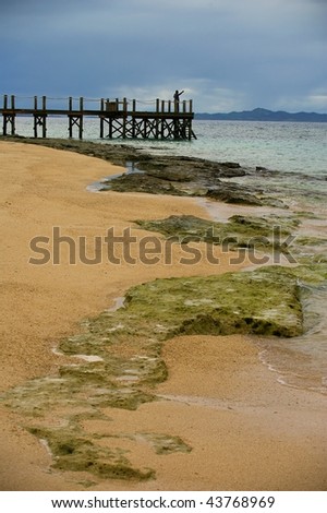 Dramatic backdrop of rocky outcrops on the Fiji coral coast islands with fisherman on pier