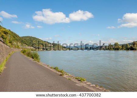 Bike path in Germany along the Rhine. The bike path goes along the river Rhine. On the other side a small castle. Sunny day, blue sky and white clouds.