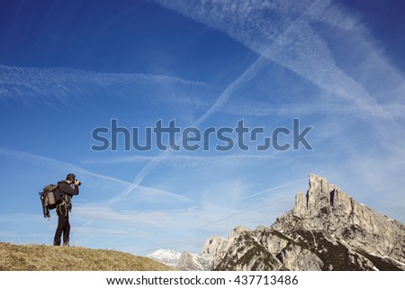 Hiker photographer taking photos on a mountain top in alpine landscape, enjoying the view. Active lifestyle, natural environment, freedom and sports concept. Big blue sky in the background. 
