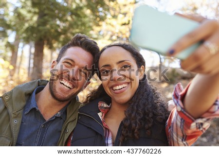 Laughing mixed race couple taking a selfie in a forest